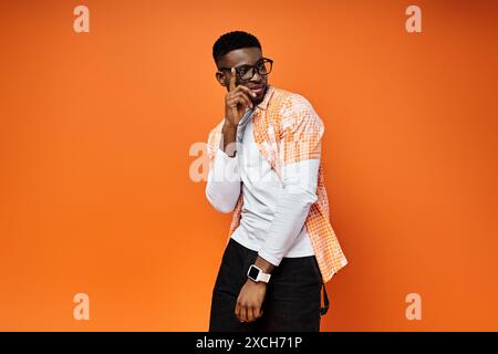 Homme afro-américain à la mode dans des lunettes et un pantalon noir pose en toute confiance sur fond orange vibrant. Banque D'Images