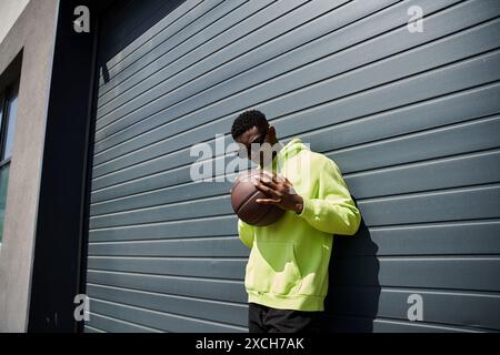 Homme afro-américain élégant en sweat à capuche jaune, basket-ball saisissant. Banque D'Images