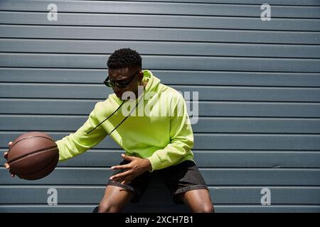 Jeune homme d'ascendance africaine dans un sweat à capuche vert vif tenant un basket-ball. Banque D'Images