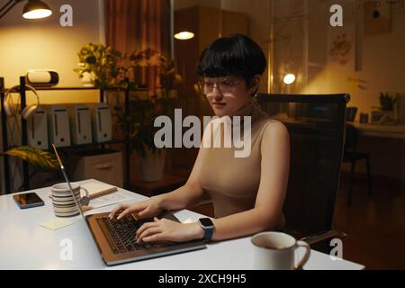 Jeune directeur du marketing travaillant sur ordinateur portable dans le bureau sombre la nuit Banque D'Images