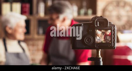 Couple senior souriant tout en filmant la vidéo de cuisine dans Home Kitchen Banque D'Images