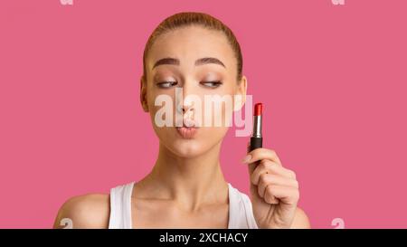 Jeune femme appliquant Red Lipstick sur fond rose Banque D'Images