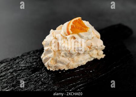 Rouleau de meringue. Protéines fouettées et sucre, garniture - fromage à la crème à base de fromage à pâte molle et de crème sur une planche à découper noire Banque D'Images