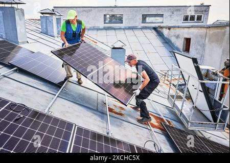 Ouvriers construisant le système de panneau solaire sur le toit en métal de la maison avec l'aide de l'ascenseur de grue. Deux installateurs hommes transportant le module solaire photovoltaïque à l'extérieur. Concept de génération d'énergie renouvelable. Banque D'Images