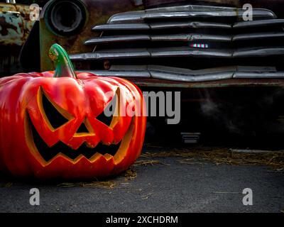 Halloween Jack o Lantern Pumpkin avec un visage maléfique effrayant, placé sur le sol près de la vieille voiture vintage dans le garage avec espace de copie. Joyeux jour d'Halloween Banque D'Images