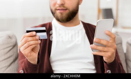 Homme tenant un téléphone intelligent et une carte de crédit, recadré Banque D'Images