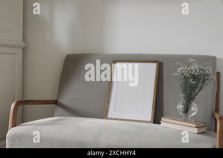 Intérieur scandinave minimal. Maquette de cadre en bois vierge. Vase en verre avec fleurs de limonium sèches, vieux livres. Élégant canapé en lin du milieu du siècle Banque D'Images