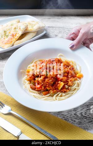 Un bol de ragu bolognaise servi sur un lit de spaghettis. Une portion est placée sur une table dans un bol blanc profond et servie avec du pain à l'ail Banque D'Images