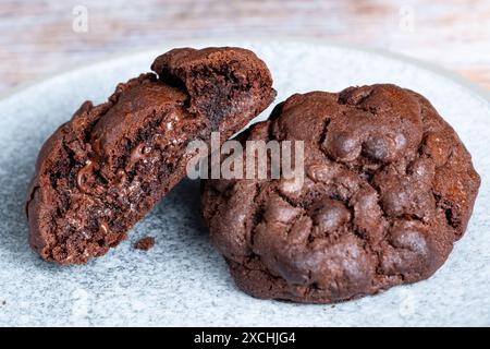 Biscuits chauds au chocolat de style New York fraîchement cuits, suintant du chocolat. Les biscuits sont servis sur une assiette avec une coupe en deux pour montrer une riche garniture de chocolat Banque D'Images