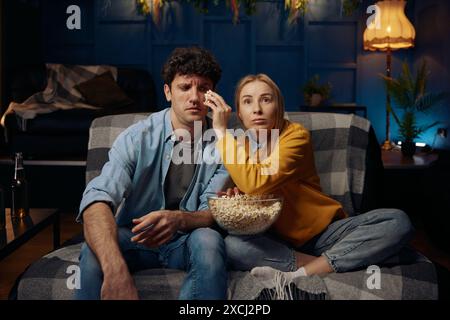 Un jeune couple est assis sur un canapé en train de manger du pop-corn Banque D'Images