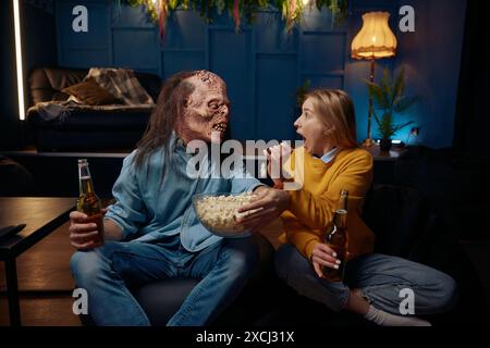 Femme choquée et homme portant un masque de monstre regardant le film avec pop-corn ensemble, couple impressionné Banque D'Images