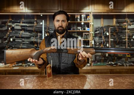 Vendeur d'homme mûr démontrant l'arme debout au comptoir dans le magasin d'armes Banque D'Images