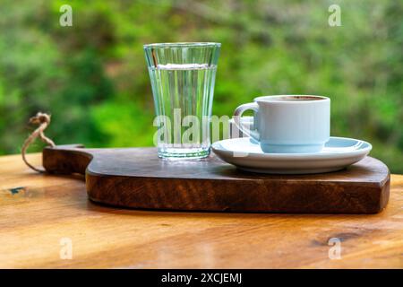 Présentation de café turc avec des galets de chocolat et un verre d'eau, sur fond de feuillage luxuriant dans la nature. Banque D'Images