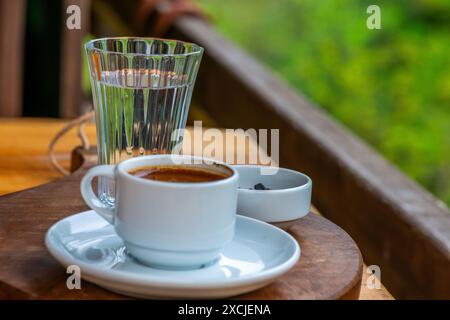 Présentation de café turc avec des galets de chocolat et un verre d'eau, sur fond de feuillage luxuriant dans la nature. Banque D'Images