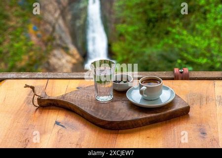 Présentation de café turc avec du chocolat de galets et un verre d'eau, sur fond de cascade sereine dans la nature. Banque D'Images