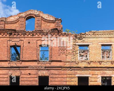 Le bâtiment abandonné en briques rouges est en rénovation, le mur de façade avec des fenêtres vides est sous le ciel bleu Banque D'Images