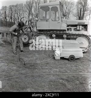 1980s, dehors dans un champ, un homme jet lavant un tracteur à chenilles Fiat 100C, Angleterre, Royaume-Uni. Bien que mieux connue comme l'un des principaux fabricants de voitures, Fiat était en fait l'un des principaux constructeurs mondiaux de tracteurs à chenilles. Banque D'Images