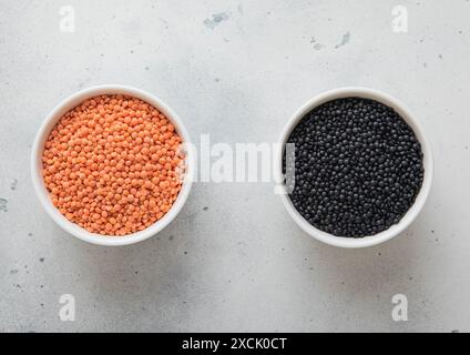 Bols en céramique avec des graines de lentilles orange sèches crues et noires sur la table de cuisine. Banque D'Images