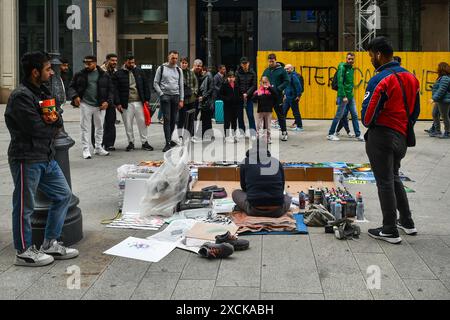 Vue arrière d'un artiste de rue créant des peintures avec des bombes aérosol sur le trottoir dans la Piazza dei Mercanti centrale, avec les gens regardant, Milan, Italie Banque D'Images