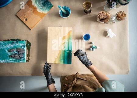 Artiste féminine créant l'image de la mer sur une planche de toile en bois, travaillant sur un établi propre et soigné. Banque D'Images