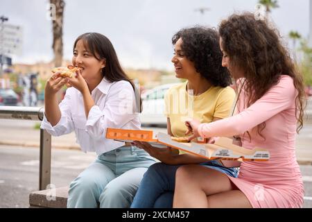 Trois femmes sont assises sur un banc en train de manger de la pizza Banque D'Images