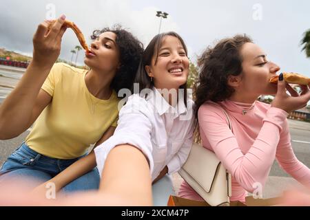 Trois femmes mangent de la pizza ensemble, souriant et profitant de leur repas Banque D'Images