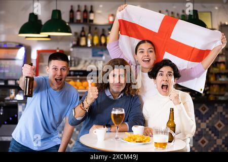 Groupe d'amis, supporters sportifs acclamant l'équipe favorite avec drapeau de l'Angleterre tout en regardant le match à la télévision dans le bar Banque D'Images