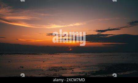Une scène de plage tranquille au coucher du soleil avec un ciel vibrant se reflétant sur les eaux calmes. Le cadre serein capture la transition paisible du jour à la nuit, soulignant la beauté et la tranquillité de la nature. Banque D'Images