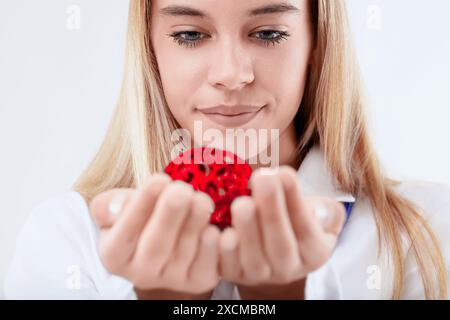 La scientifique tient soigneusement un modèle de molécule rouge dans ses mains, son expression concentrée et intriguée par le concept scientifique qu'elle représente Banque D'Images