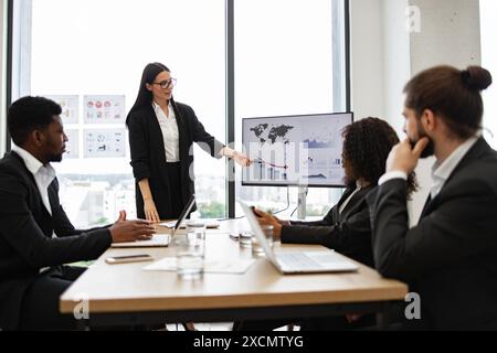 Femme d'affaires présente le rapport à ses collègues près des graphiques sur le moniteur Banque D'Images