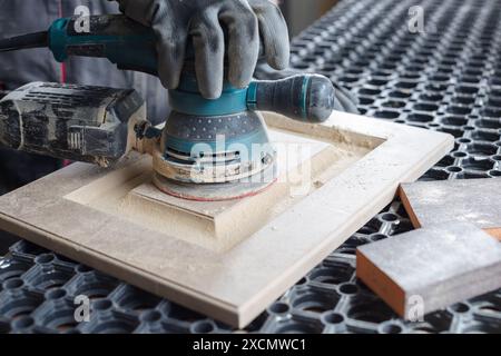 Un menuisier masculin sabre les façades de meubles en bois avec une ponceuse dans une usine de production de meubles, concept de traitement du bois Banque D'Images