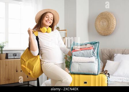 Jeune femme enceinte avec des sacs emballés prêts pour les vacances dans la chambre Banque D'Images