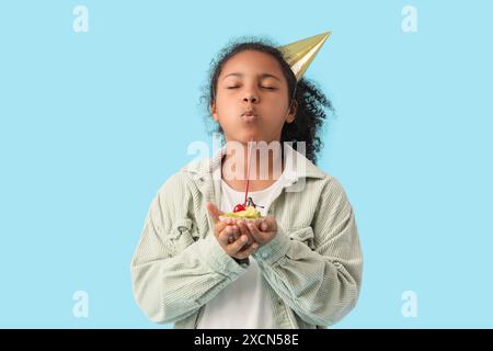 Jeune fille afro-américaine avec gâteau d'anniversaire soufflant la bougie sur fond bleu Banque D'Images