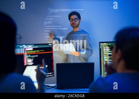 le développeur asiatique dirige la présente session de révision de code, pointant le code projeté sur le mur avec des collègues travail d'équipe et partage de connaissances dans le logiciel Banque D'Images