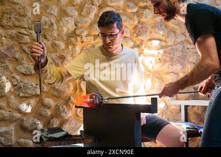Deux hommes caucasiens travaillant ensemble dans un atelier de soufflage de verre créant une cruche en verre soufflé Banque D'Images