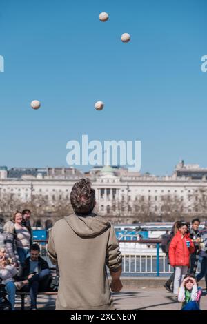 Domenyk la Terra jongle aux balles devant le National Theatre, Southbank London, tandis que les gens regardent. De l'autre côté de la Tamise se trouve Somerset House. Banque D'Images