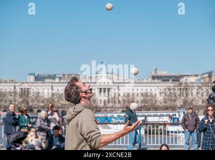 Domenyk la Terra jongle aux balles devant le National Theatre, Southbank London, tandis que les gens regardent. De l'autre côté de la Tamise se trouve Somerset House. Banque D'Images