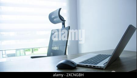 souris d'ordinateur gros plan à proximité ordinateur portable et clavier argenté, chaise et fond de fenêtre, concept de bureau Banque D'Images