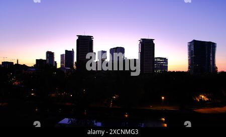 L'horizon de la ville est éclairé la nuit, avec le coucher du soleil en arrière-plan. Les bâtiments sont grands et les lumières sont allumées, créant une ambiance chaleureuse et tonique Banque D'Images