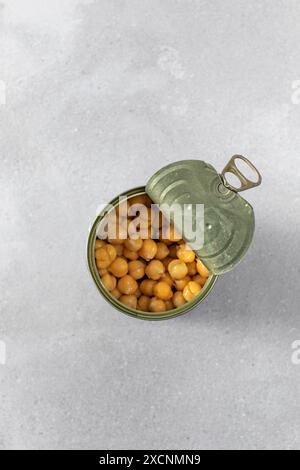 Boîte de conserve ouverte avec de savoureux pois chiches conservés sur gris clair Banque D'Images