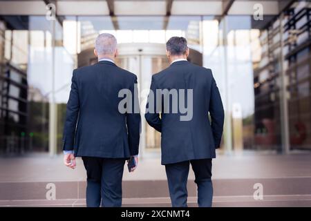 Vue arrière de deux hommes d'affaires marchant pour entrer dans l'immeuble de bureaux à l'extérieur. Banque D'Images