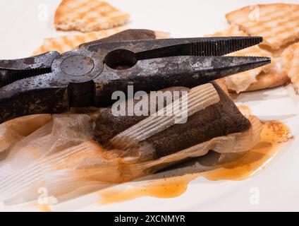 Pince pointue rouillée reposant sur le dessus d'un sachet de thé usagé avec des biscuits cassés dispersés à travers la scène. Pause thé concept. Banque D'Images