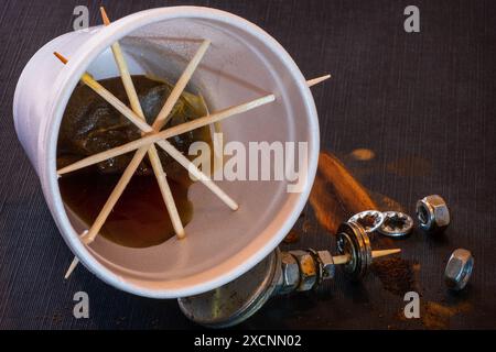 Tasse jetable en polystyrène blanc avec sachet de thé et thé disposés sur fond sombre avec des écrous rouillés et des boulons. Banque D'Images