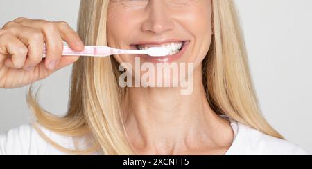 Femme aux cheveux blonds se brossant les dents avec une brosse à dents, rognée Banque D'Images