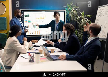 Groupe de relations publiques créant des campagnes publicitaires marketing et des activités promotionnelles dans une salle de conférence, collaborant sur le plan de développement. Spécialistes examinant les tendances des ventes sur un tableau interactif. Banque D'Images