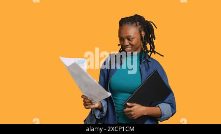 Employé comptable travaillant les yeux roulants, regardant les pages de rapport, se sentant ennuyé, isolé sur fond de studio. Jeune fille frustrée après avoir lu des documents toute la journée tout en résolvant des tâches, caméra A. Banque D'Images