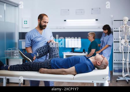 Spécialiste de la santé massant les muscles des jambes du patient senior, en utilisant la médecine alternative pour augmenter la mobilité dans la clinique de réadaptation. Ostéopathe masculin faisant de la physiothérapie pour un vieillard retraité. Banque D'Images