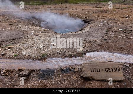 Litli Geyser (Litli Geysir) mijotant et fumant avec un panneau d'information, zone géothermique de la vallée Haukadular en Islande, pas de gens. Traduction : Litli Banque D'Images