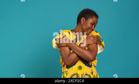 Jeune femme confiante représentant son ethnie africaine en portant une robe indigène tribale avec des éléments floraux en studio. Douce fille naturelle embrassant elle-même étant fière de ses origines. Caméra A. Banque D'Images