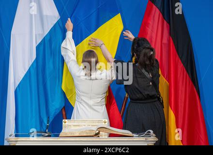 Munich, Allemagne. 18 juin 2024. Le personnel du Département du protocole de la Chancellerie d'État de Bavière ajuste les drapeaux de Bavière (de gauche à droite), de Roumanie et d'Allemagne après la réunion conjointe du cabinet avec les cabinets roumain et bavarois dans la capitale de l'État. Crédit : Peter Kneffel/dpa/Alamy Live News Banque D'Images